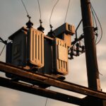 Close-up of an electrical transformer on a utility pole against a sunset sky.